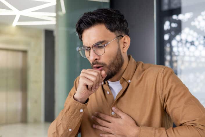 A man coughing, illustrating how genetic factors can affect lymphocyte count and immune response.