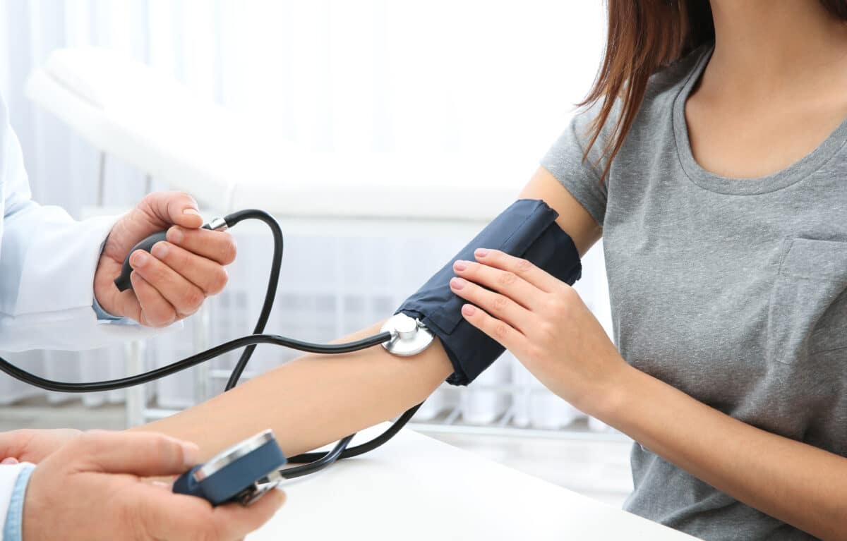 Woman checking her blood pressure with a digital monitor, symbolizing the importance of understanding genetics in high blood pressure.