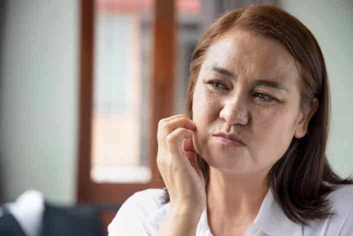 Woman scratching her face, symbolizing lupus symptoms and the genetic factors behind the autoimmune disease.