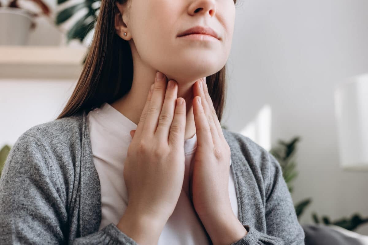 An image of a woman gently touching her throat, checking for signs of thyroid enlargement or goiter which may relate to Pendred Syndrome