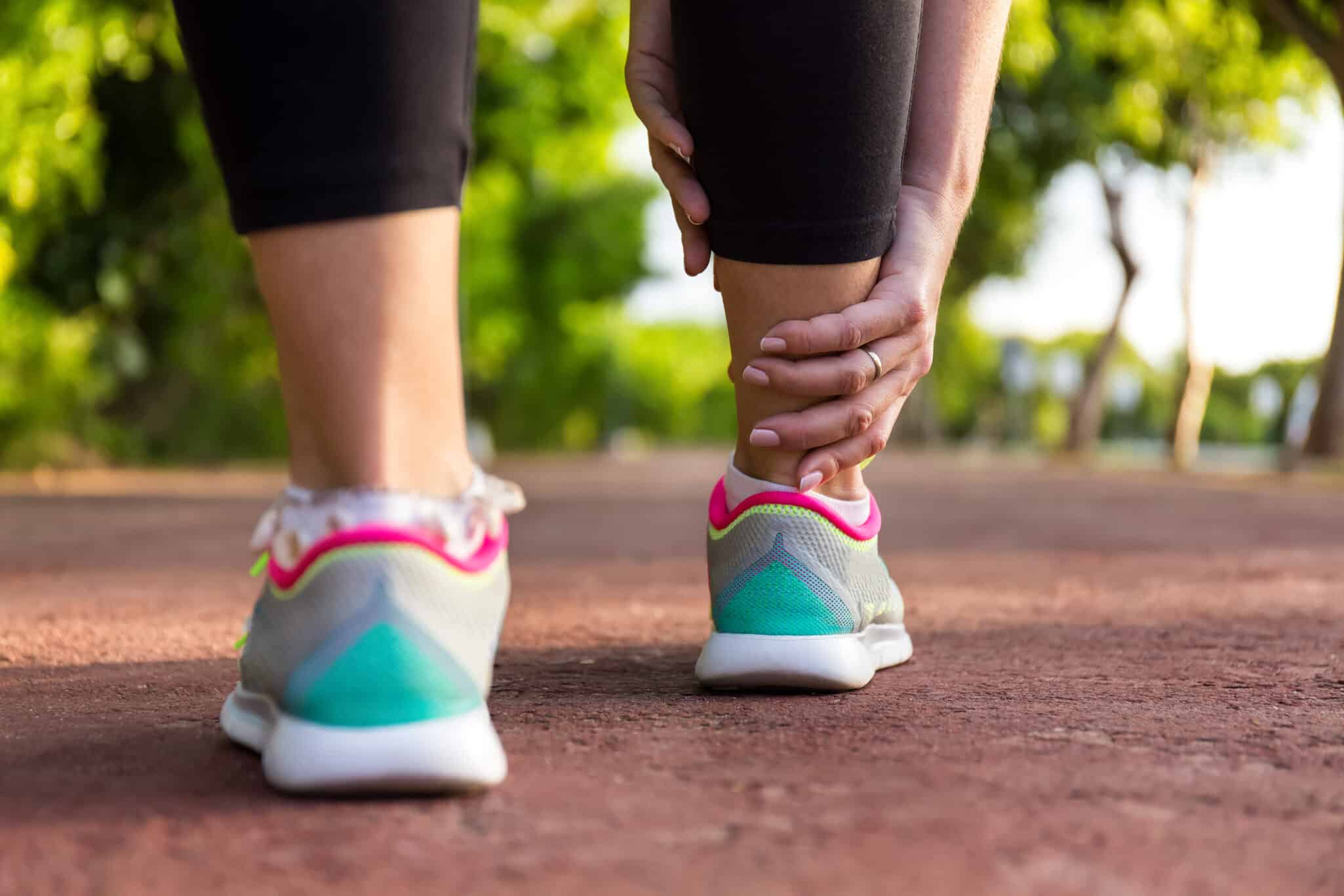 Image of a person holding the back of their leg in pain, focusing on the Achilles Tendinopathy area.