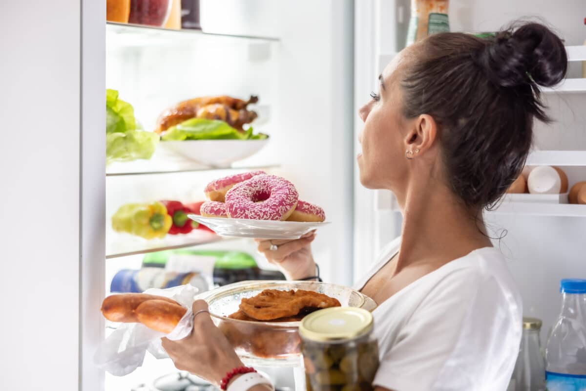 Woman reaching into refrigerator for multiple food items, representing genetic influence on hunger response control.