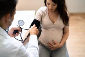 Doctor monitoring a pregnant woman with a stethoscope, highlighting care for potential genetic risk of preeclampsia