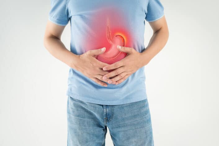 This image shows a man holding his stomach in visible discomfort, symbolizing one of the common symptoms of pernicious anemia.