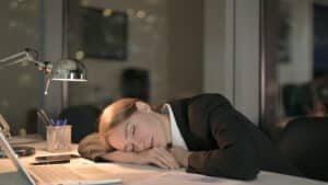 Woman asleep at her desk during work, illustrating excessive daytime sleepiness — a key symptom of narcolepsy, which may have genetic links.