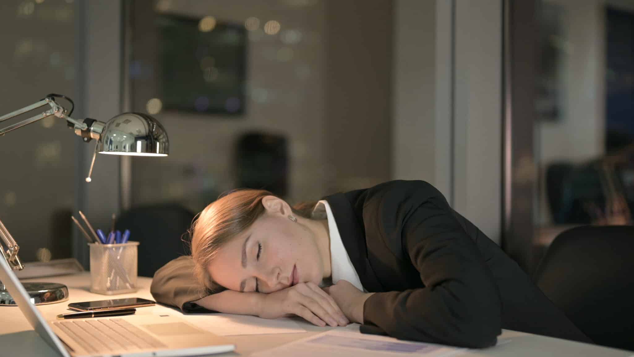 Woman asleep at her desk during work, illustrating excessive daytime sleepiness — a key symptom of narcolepsy, which may have genetic links.